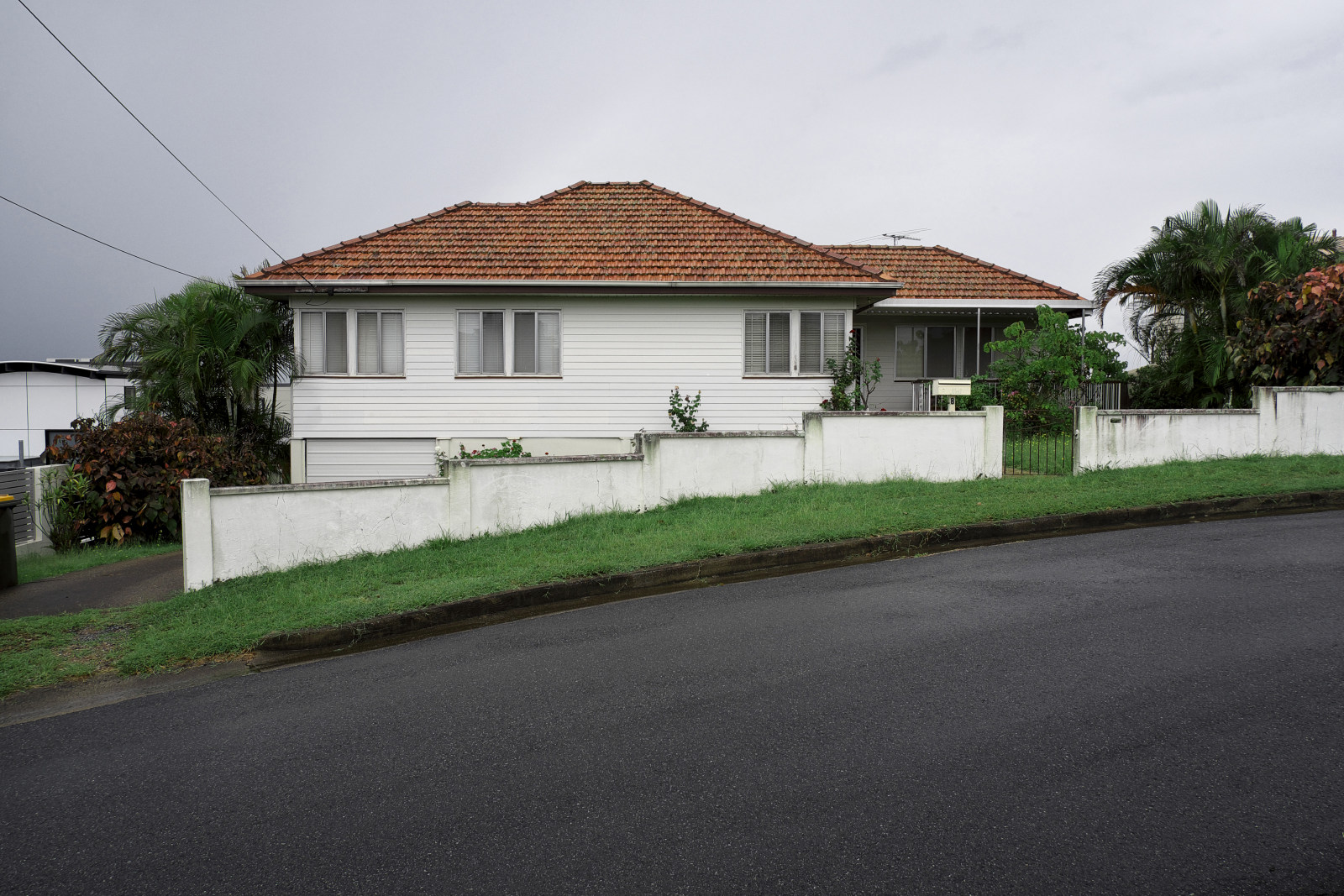 Lowset weatherboard home, curved stucco fence, Seven Hills. Brisbane vernacular architecture.