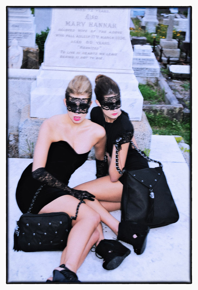 Two models on a cold marble slab at an ocean front cemetery in a blurry gothic fashion shot.