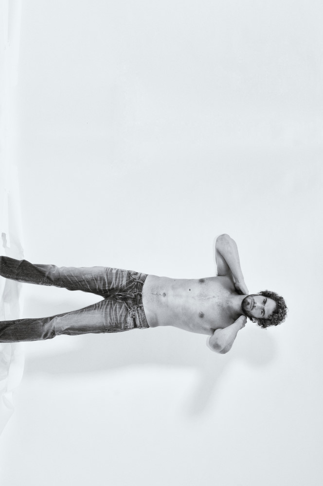 Distressed black denim jeans photographed in the studio for a menswear fashion campaign, image presented sideways.