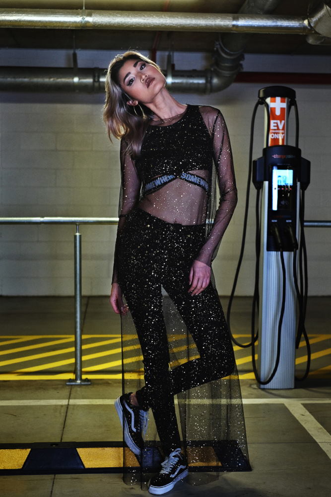 Fashion marketing photograph, a sheer black sheath dress over activewear crop top and leggings; Parking garage photoshoot in Sydney for Somewhere Label. Photography by Kent Johnson