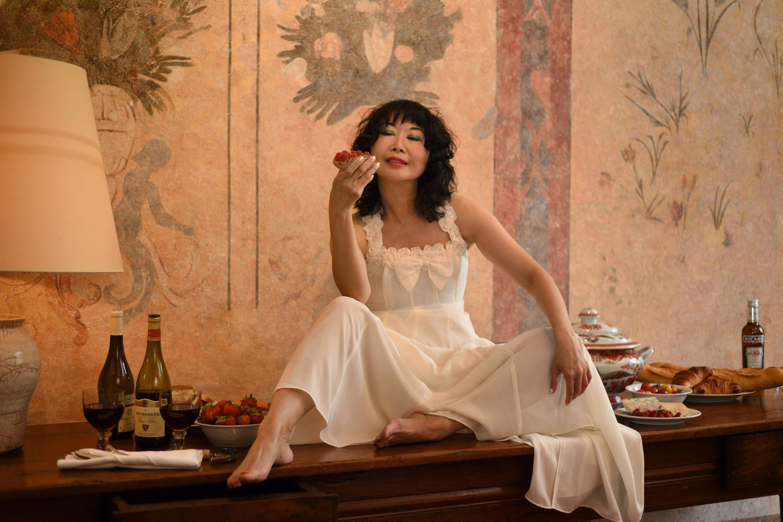 Vivienne sitting on an oak table with a picnik of local French produce, Chateau Bagnols, Bagnols France. Photography by Kent Johnson for White Caviar Life.