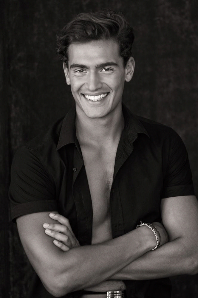 Male model smilling mid shot, black open shirt against black backdrop in studio.