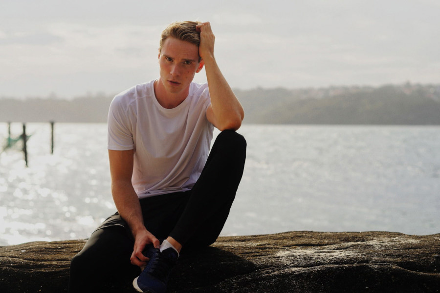 Male model sitting by waters edge Sydney Harbour Park.