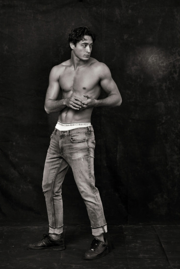 Studio portrait of a muscular male model photographed against a black background.