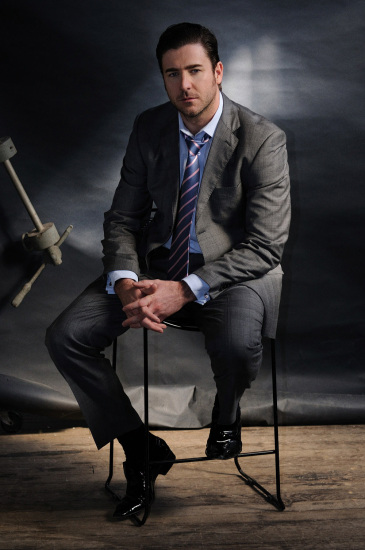 Man in a suit, loose collar and tie sitting casually in the studio.
