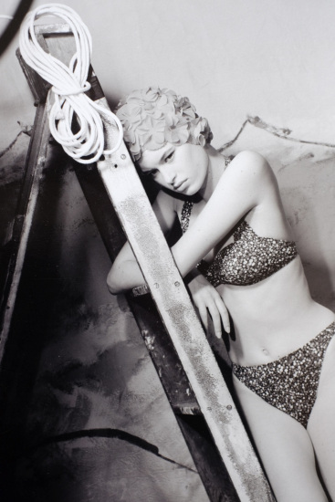 Pouting young woman in a bikini. Swimwear shot in the studio against a painted modernist seascape (Not menswear...)