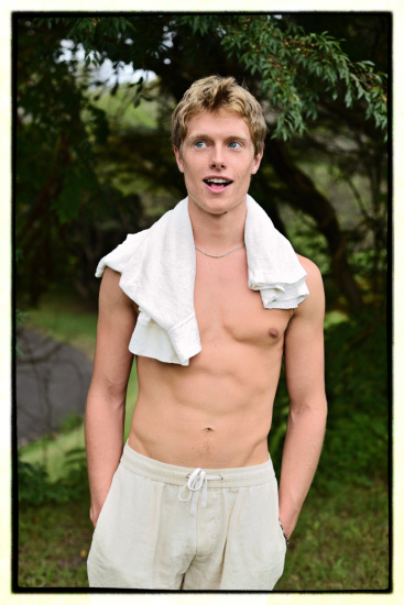Young man in a park, topless with a tee shirt around his neck.
