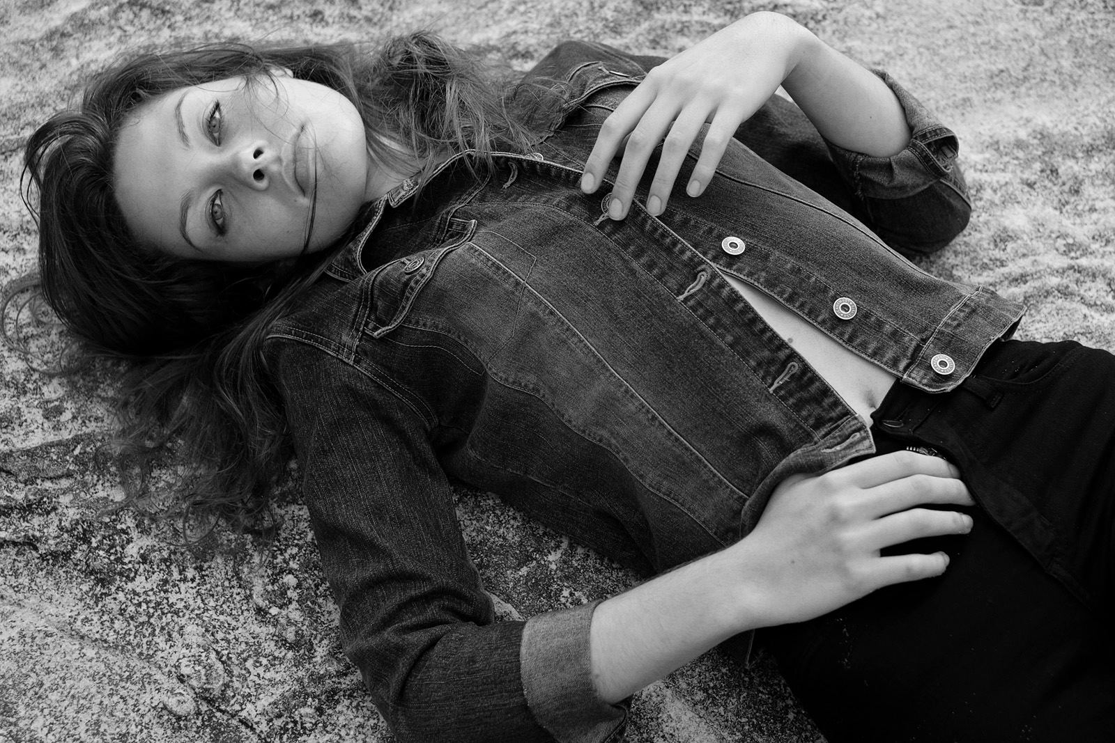 Modelling portfolio, black and white mid shot of model lying on the beach in a demim jacket.