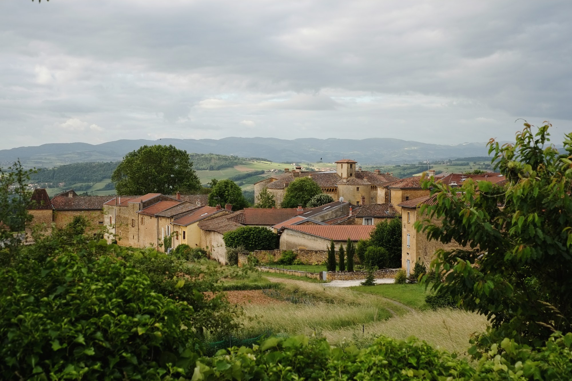 Travel photography - A scenic landscape of hills, vineyards, the Pigeonnier and Château de Bagnols. Part of the Beaujolais wine region, Arrondissement: Villefranche-sur-Saône, France. Photography by Kent Johnson.