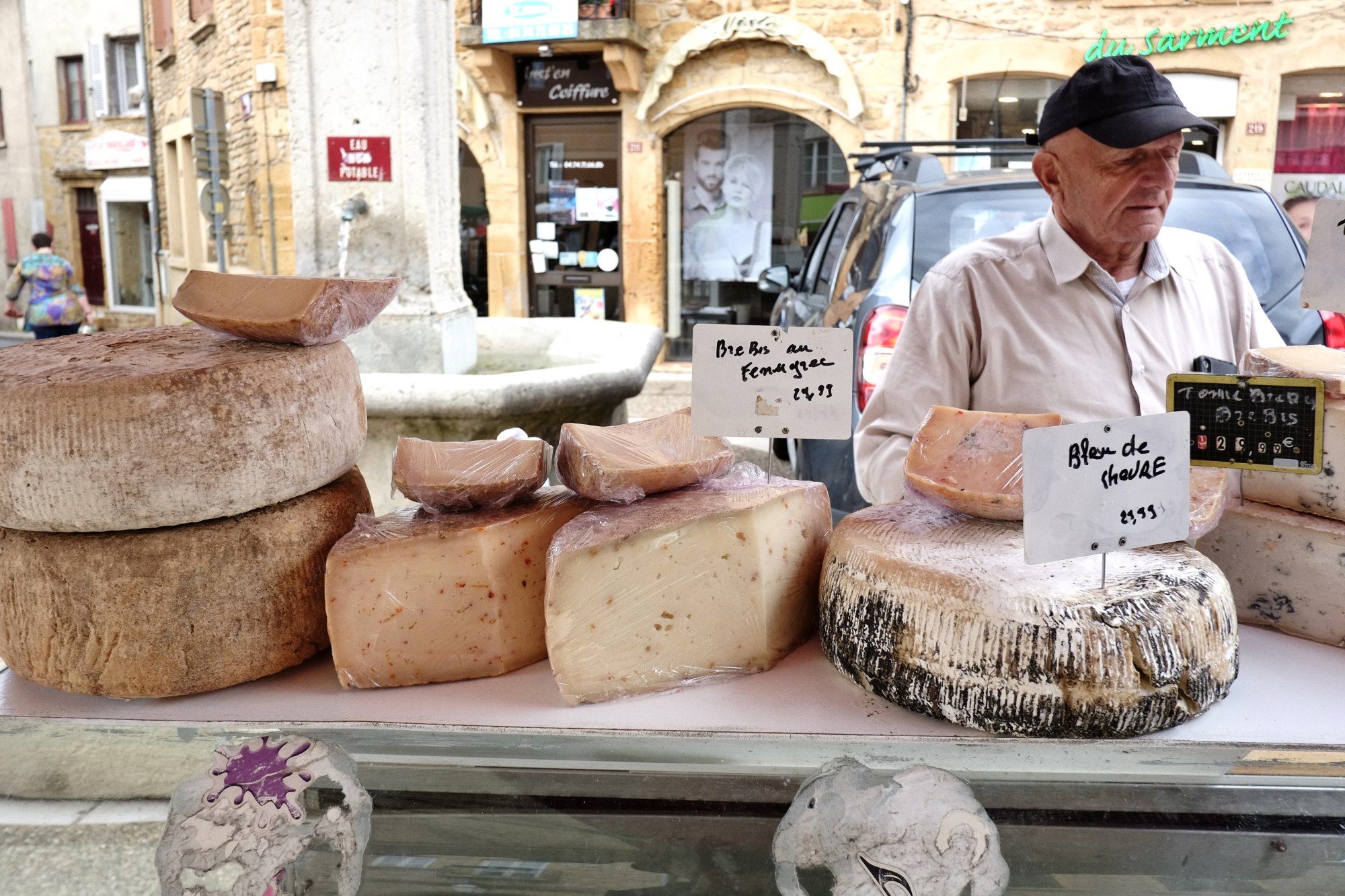 A fromage vendor at his stall, market day in Le Bois-d'Oingt. Food and travel lifestyle photography by Kent Johnson.