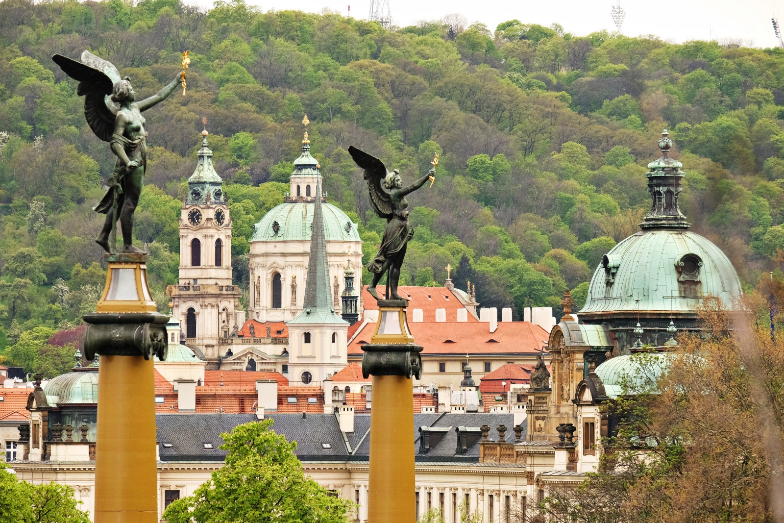 Winged victory statues dominate the view across historic Malá Strana and St. Nicholas Church to Petřín Gardens and the Petřín park