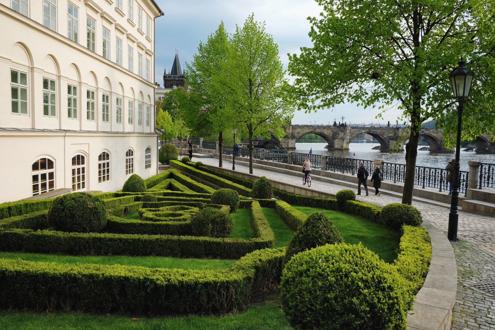 A small park with a low hedge topiary maze with the Charles bridge in the background. Travel photography by Kent Johnson.