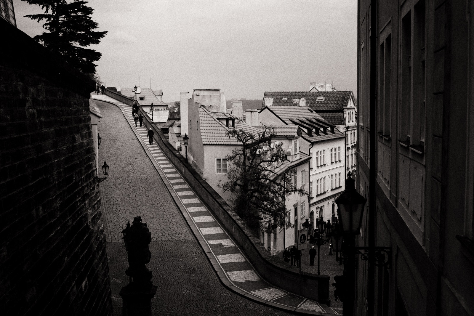 A view from Radnické schody & Ke Hradu, to Old Town, people walking up the pretty paved street to Prague castle with a backdrop of the red roofs.