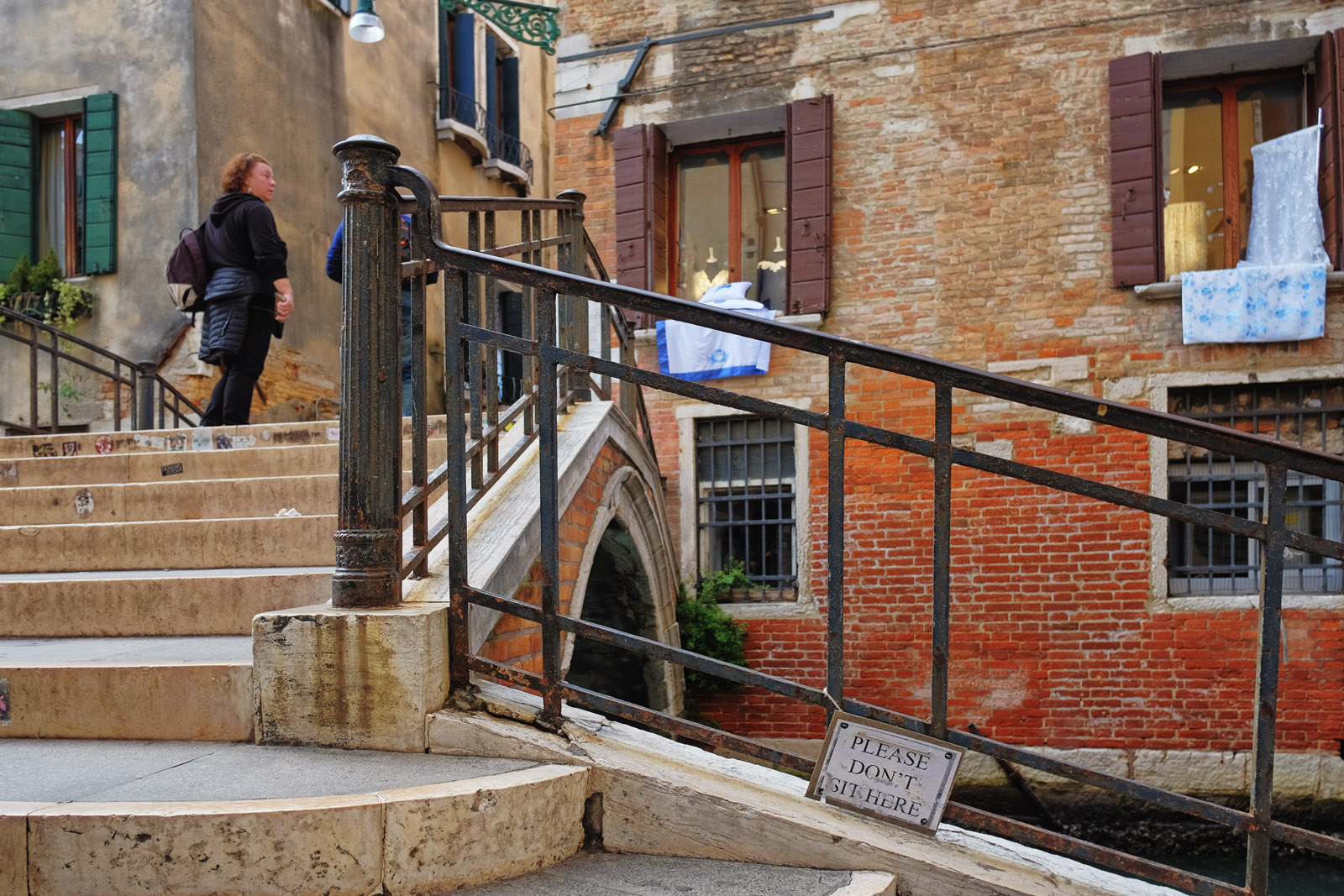 A sign on the steps of a Venice bridge asking tourists not to sit on them, a sign of over tourism.